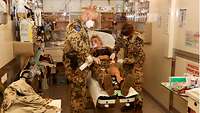 Zwei Soldaten stehen neben einer Krankentrage, auf der eine Soldatin liegt