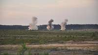 Durch die Explosion von Panzerabwehrminen bilden sich drei große Rauchwolken im Gelände