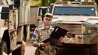 Ein Soldat steht mit einer Mappe vor zwei Bundeswehrfahrzeugen