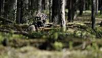 Ein Soldat sitzt mit einem Gewehr in einem Erdloch und beobachtet das Vorfeld