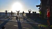 Mehrere Soldatinnen und Soldaten treiben am frühen Morgen Sport auf dem Flugdeck eines Schiffes