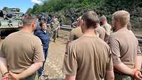 Eine blau gekleidete Zivilistin steht vor Soldaten in beigen T-Shirts, die sich um sie herum versammelt haben.