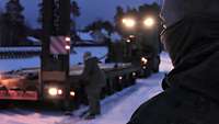 Über die Schulter eines Soldaten ist der beleuchtete Auflieger eines Lastwagens zu sehen