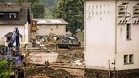 Ein Bagger und ein Bergepanzer räumen Schutt aus einer Straße. 