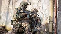 Zwei bewaffnete KSK-Soldaten an einer Hauswand beobachten kniend die Umgebung 
