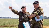 Zwei Soldaten stehen auf einem Feld in Litauen und blicken in die Ferne. Ein Soldat zeigt in eine Richtung.