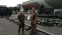 Zwei Soldaten halten ein Dokument zwischen sich, im Hintergrund Tankanlagen vor der Außenwand einer Tribüne