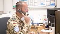 Ein Soldat sitzt am Schreibtisch und telefoniert. Er schaut dabei auf einen Computerbildschirm