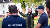 Ein Militärpfarrer der Bundeswehr steht mit ausgebreiteten Armen vor Bundeswehr-Feuerwehrmännern