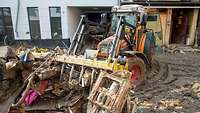 Ein Traktor mit Greifschaufel hat Unrat im Hochwassergebiet in der Schaufel