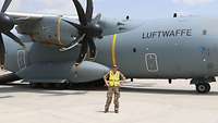 Vor einem Transportflugzeug vom Typ A400M steht ein Soldat mit Warnweste