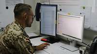 Ein Soldat sitzt an seinem Schreibtisch vor einem Bildschirm