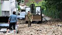 Ein Soldat geht über ein Geröllfeld, das eine Straße bedeckt. Im Hintergrund stehen Häuser und ein Gabelstapler.