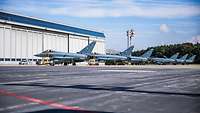 Six combat airplanes in front of a large hangar