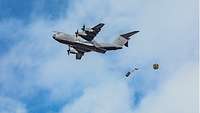 An object attached to a parachute is dropped from the cargo hatch of a military transport aircraft