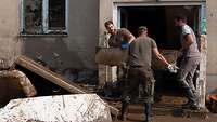 Zwei Soldaten und ein weiterer Mann räumen Sperrmüll aus einem Haus
