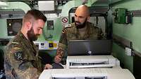 Zwei Soldaten stehen an einem Drucker in einem Container und sprechen mit einander