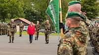 Soldaten halten einen grünen Wimpel grüßen militärisch grüßen. Drei Personen schreiten die Front ab.