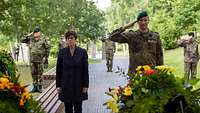 Ministerin Kramp-Karrenbauer steht mit Soldaten vor Blumenkränzen im Wald der Erinnerung