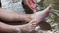 Die Unterschenkel einer Person liegen im Wasser, eine Hand gießt zusätzlich Wasser über die Füße