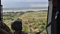 Blick aus der Seitentür eines Helikopters auf die grüne Landschaft mit dem Fluss Niger.