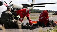 Sanitäter arbeiten an einem Übungsverletzten. Im Hintergrund ist eine Transall zu sehen.