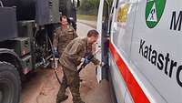 Zwei Soldaten an einem Straßentankwagen betanken ein ziviles Hilfsfahrzeug