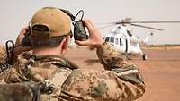 Ein Soldat steht vor einem weißen Hubschrauber und nimmt seinen Gehörschutz ab