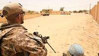 Ein Soldat sichert mit einem Gewehr eine Einfahrt in einem afrikanischen Dorf