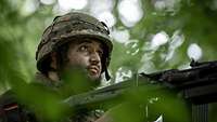 Soldat mit Tarnschminke auf seinem Alarmposten mit einem Maschinengewehr 3 auf einem abgetarnten geländegängigen Lkw.