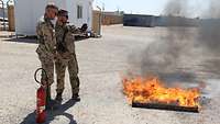 Ein Soldat erklärt einem weiteren Soldaten das richtige Vorgehen beim Bekämpfen eines Brandes