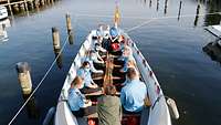 Ein Dutzend Menschen in Uniform sitzen in einem kleinen Ruderboot und unterhalten sich mit der Ministerin.