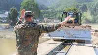 Ein Soldat weist mit Handzeichen ein Räumfahrzeug beim Überqueren einer Behelfsbrücke ein