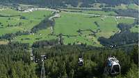 Eine Kabinenbahn fährt auf einen Berg darunter der Blick ins Tal 