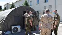 International soldiers stand in front of a large military tent. Two of them look inside. 