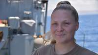 Porträt: Eine Soldatin lächelt in die Kamera. Im Hintergrund das Meer 