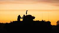 Schützenpanzer in Umrissen bei Sonnenaufgang. Auf dem Panzer sitzen zwei Soldaten.