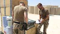 Zwei Soldaten stehen vor einigen Kisten mit Material