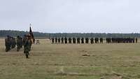 Zahlreiche Soldaten stehen auf einem grünen Feld nebeneinander in Formation. 