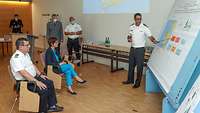 Lieutenant Commander Costa standing in front of a plan in class presenting an operational scenario