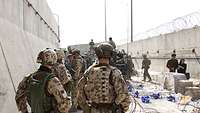 Soldaten kontrollieren Personen in einem mit Mauern und Stacheldraht eingegrenzten Zugangsbereich am Flughafen in Kabul