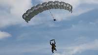 Zwei Soldaten schweben gemeinsam an einem Fallschirm unter blauem Himmel gen Boden.
