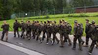 Jugendliche in Uniform marschieren in einer Gruppe eine Straße entlang.