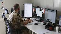 Ein Soldat sitzt am PC und tippt auf der Tastatur seines Rechners. Vor ihm stehen drei Monitore