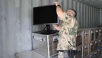Ein Soldat überprüft einen Monitor. Dieser steht auf einer von vielen Metallkisten