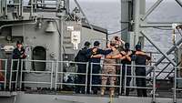 Mehrere Marinesoldaten auf dem Oberdeck eines Kriegsschiffs posieren für ein Gruppenfoto. 