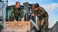 Zwei Soldaten bereiten eine Lieferung mit Essenspaketen für den Transport vor