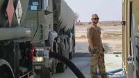 Ein Soldat steht an einer Tankanlage, um den Tankwagen aufzutanken. Hinter ihm stehen zwei Tankfahrzeuge