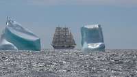 Ein weißes Segelschiff segelt durch das Meer und passiert große Eisberge.