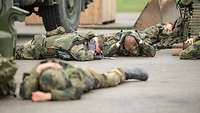 Mehrere Soldaten im Gefechtsanzug liegen auf dem Boden und halten sich die Ohren zu.